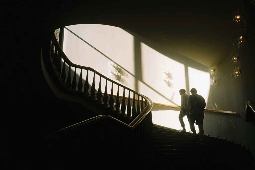 Two figures ascend a staircase in sunlight.